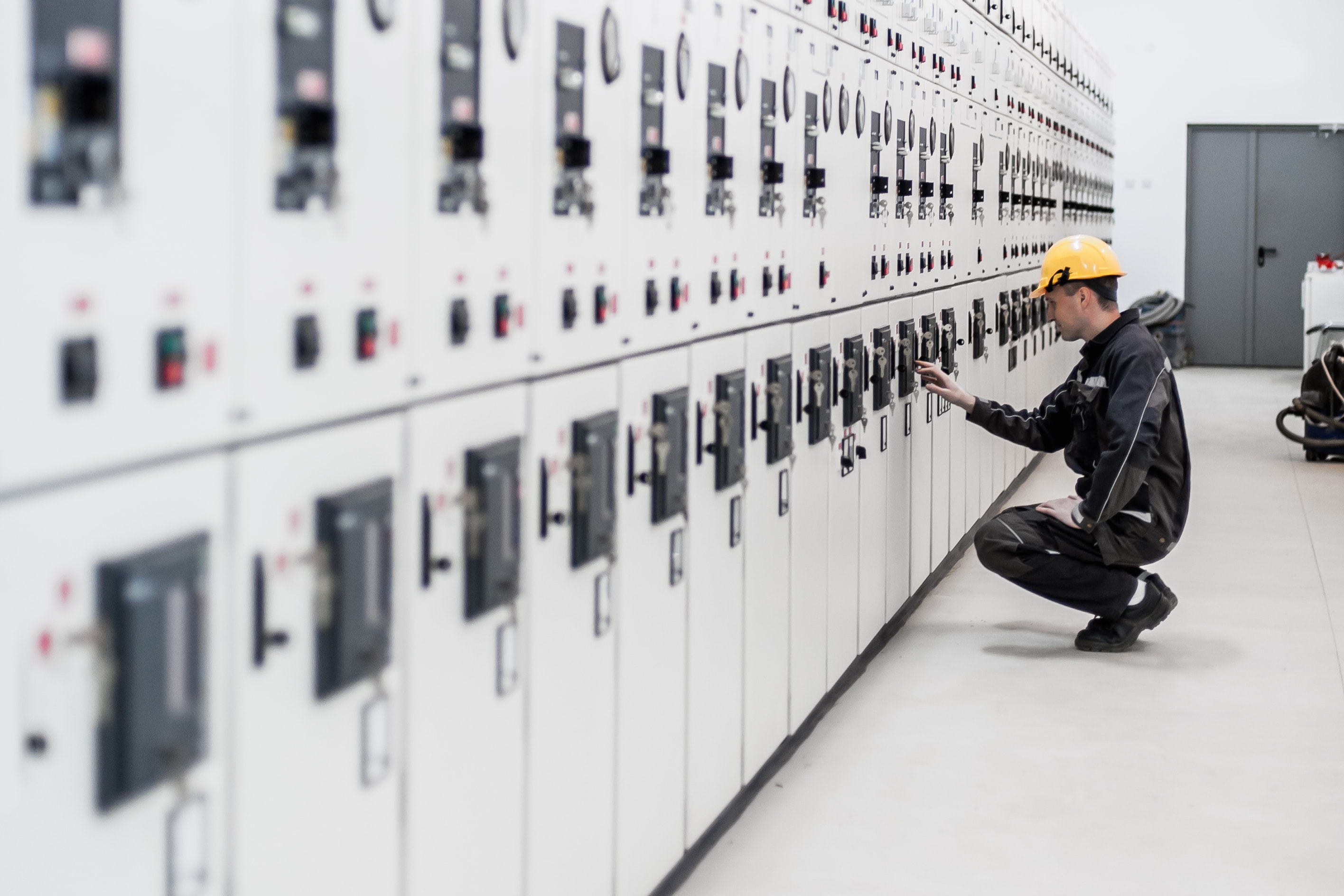 Electrical engineer in hard hat inspecting a white switchgear lineup during a power system study